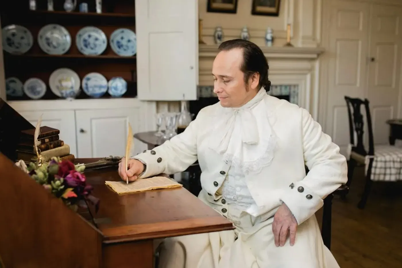 Hamilton at a historic desk with a quill pen