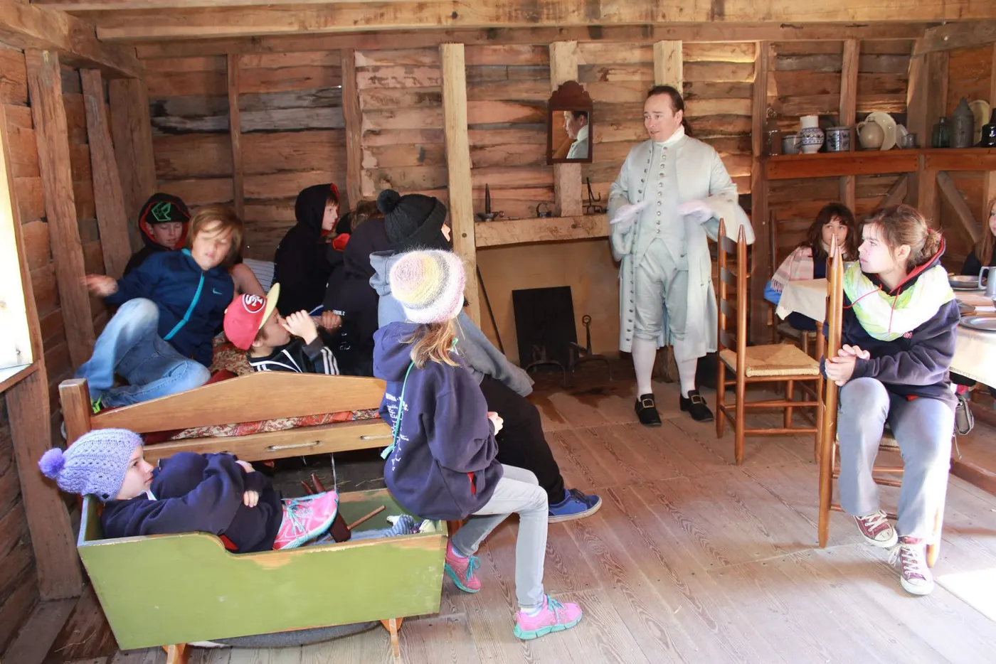 Hamilton teaching children inside a historic log cabin